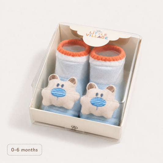 A pair of baby socks in a clear plastic gift box. The socks are light blue with orange cuffs and feature a plush bear face patch on the front with a blue nose. A1S Baby Cartoon Cotton Socks Imported