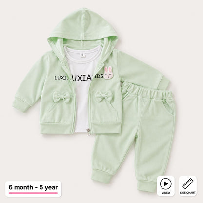 A baby girl's two-piece tracksuit set in pale mint green, featuring a zip-up hoodie with bow details and a white t-shirt underneath, shown on a light beige background with age and informational overlays.