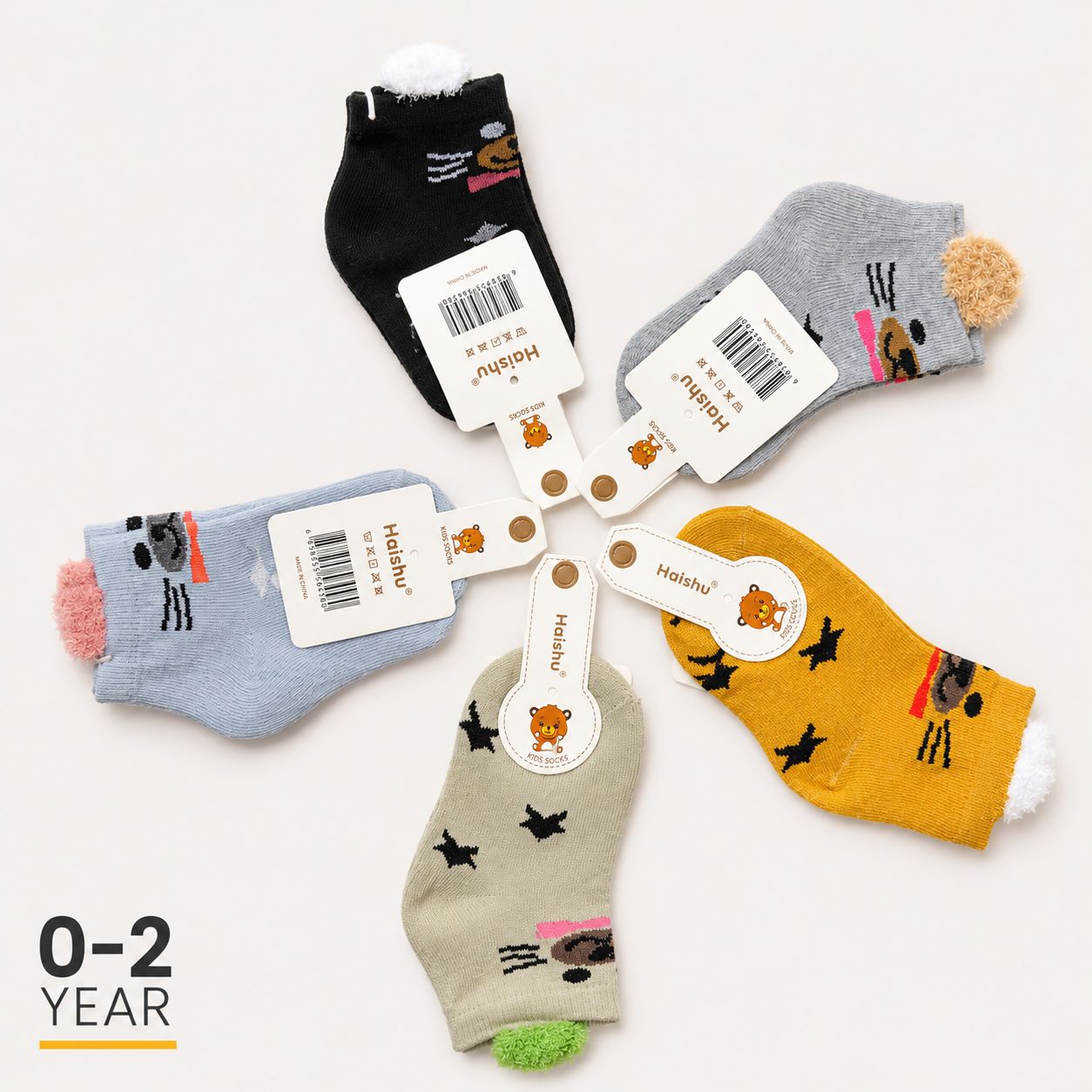 Five pairs of children's ankle socks arranged in a circle on a light beige background, each with a white paper tag attached. The socks come in black, gray, light blue, mustard yellow, and beige colors, and feature playful cartoon animal prints.