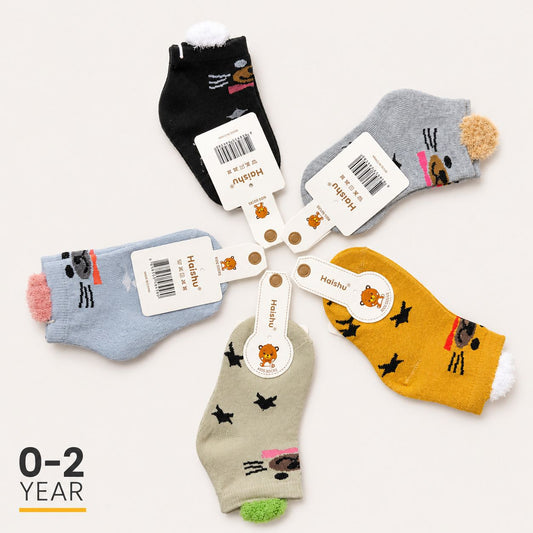 Five pairs of children's ankle socks arranged in a circle on a light beige background, each with a white paper tag attached. The socks come in black, gray, light blue, mustard yellow, and beige colors, and feature playful cartoon animal prints.