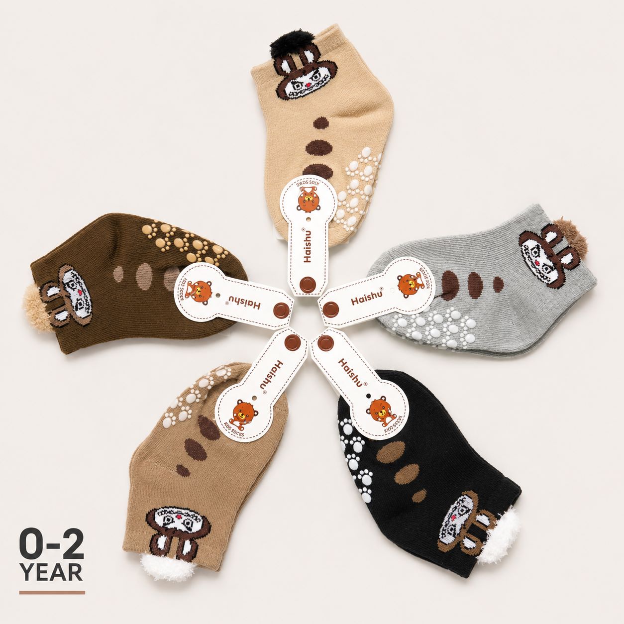 Five pairs of children's knit socks arranged in a circle on a light beige background. The socks come in tan, brown, gray, beige, and black, each decorated with paw prints, paw pads, and a cartoon bear face patch near the cuff.