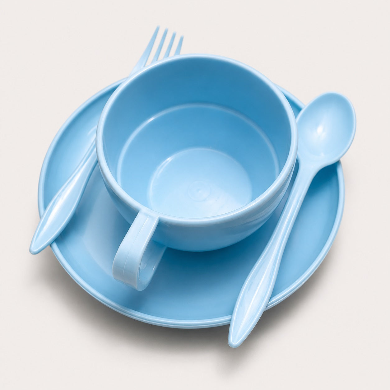Light blue plastic dinnerware set including a cup, saucer, fork, and spoon, arranged on a light beige background.
