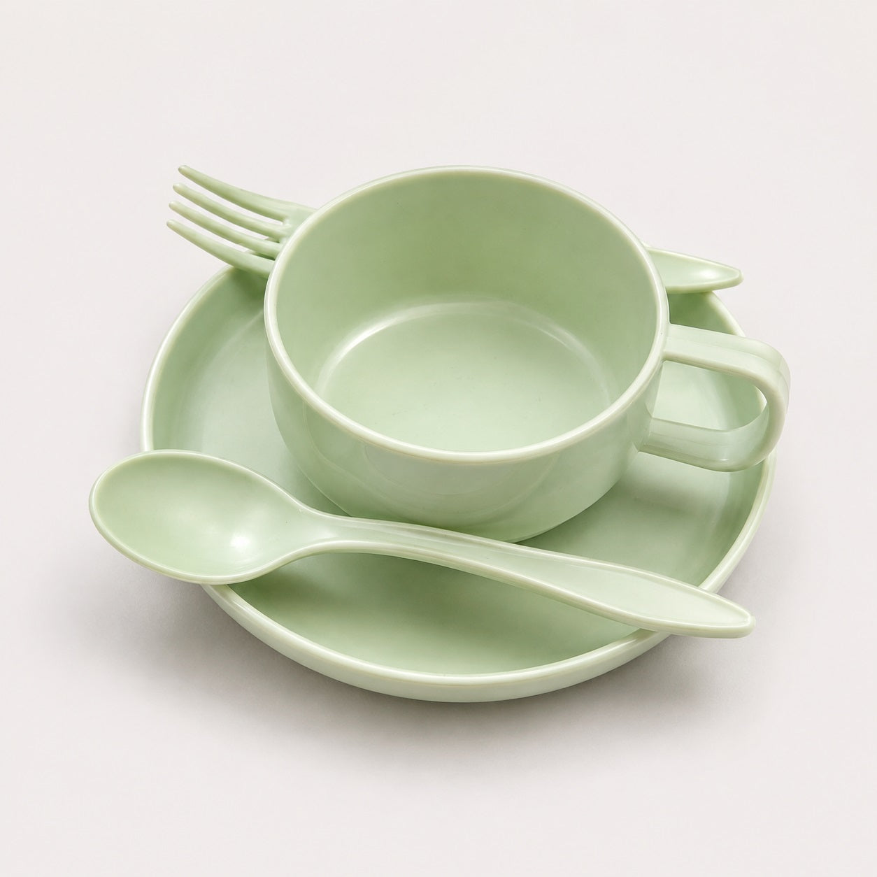 A light mint green ceramic tableware set including a cup, matching saucer, spoon, and fork, arranged on a clean off-white background.